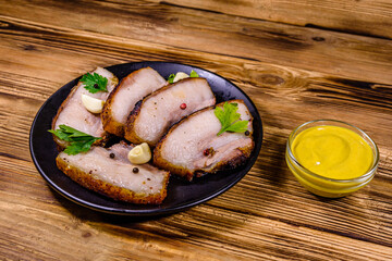 Slices of baked pork belly, garlic and parsley on a black plate