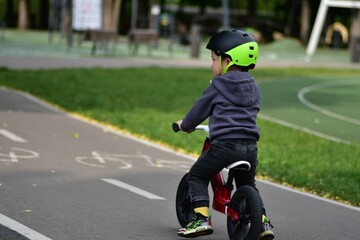 Fototapeta premium Young toddler boy riding a balance bike on a park bike path. Child wearing helmet and sporty outfit enjoys outdoor fun and physical activity on a sunny day.
