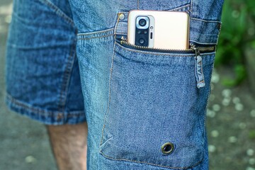 one modern with camera mobile phone lies in pocket with unbuttoned iron with slider zipper in fashion stylish blue worn men's with stripes and button denim shorts on legs day outside
