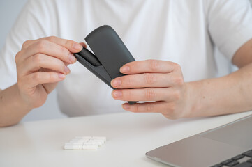 A woman takes a tobacco heating system out of a charger. Electronic cigarette.