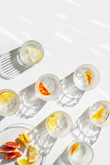 Crystal glasses with citrus slices in water on white background with rainbow reflections at sunlight, modern, minimal composition with glass cups filled with water and citrus fruit, as lemon orange