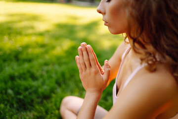 Young woman sitting in lotus pose with hands raised up on bright yoga mat. Calm woman practicing...