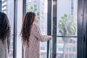 Obraz premium Digital nomad arriving at airbnb apartment with suitcase, gazing out window at city view