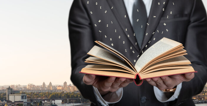Book in hands with floating letters above skyline.