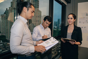 Three professionals collaborate in a modern office environment, engaging in discussion and planning.