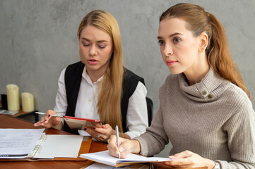 Two women engaged in a business meeting, taking notes and discussing strategies at a modern workspace.