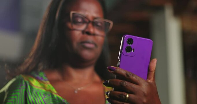 African American woman squinting at smartphone screen with puzzled expression, reacting to unexpected message in dimly lit evening environment