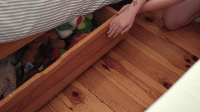 Child puts up her toys away in an under bed storage box.