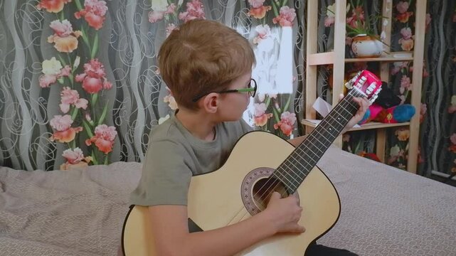 A teenage boy plays the guitar on the sofa. Active children's recreation. Let's learn to play the guitar.