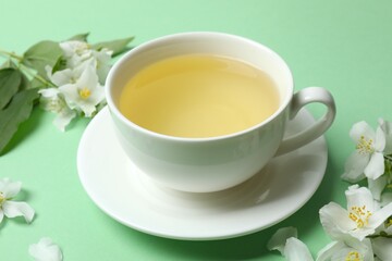 Cup of tea with jasmine flowers on green background