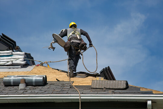 Construction Roofer Wearing Hard Hat Installing Shingles on Residential Roof Against Blue Sky