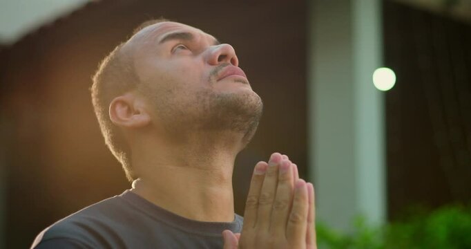 Latin American man looking upward with raised arms in expressive moment of prayer or spiritual surrender, standing outdoors in golden afternoon light