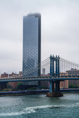 New York City skyline and buildings and the Manhattan Bridge over the East River Ferry Pier, viewed from the Brooklyn Bridge on a foggy rainy summer morning in USA