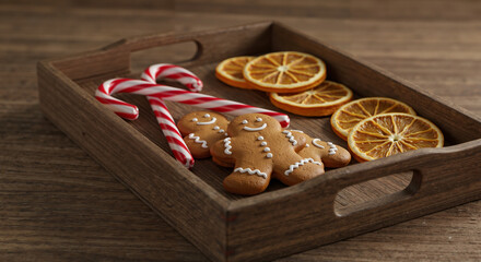 Gingerbread cookies, candy canes, and dried oranges on wooden tray  