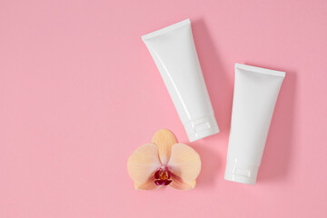 Top view of two white plastic cosmetic containers with orchid flower on pale pink background. Fashionable minimal composition of cosmetic products for face and body