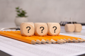 Wooden cubes with question marks on sharpened pencils over financial documents