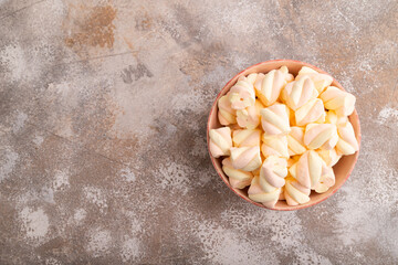Orange and pink marshmallow in ceramic bowl on brown concrete background, top view, copy space