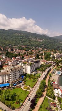 Drone video of Stresa town on Lake Maggiore, Italy, featuring historic grand hotels, bright midday sun, and cars driving along roads near the lake. Vibrant lakeside scene