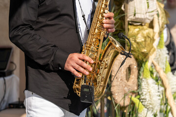 Fototapeta premium Close-up photo of a saxophonist’s hands playing the saxophone. The detailed view captures the musician’s fingers on the keys, highlighting the shine of the brass instrument and the expressive energy