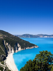 Aerial scene of Myrtos Beach in bright morning light, featuring turquoise sea and lush green coast.