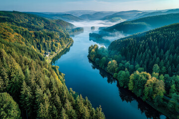 Scenic view of a winding river flowing through lush green forested hills with gentle morning mist