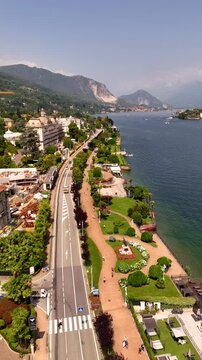 Drone video of charming towns on Lake Maggiore, Italy, including Stresa and Verbania, with historic grand hotels, sunlit roads, and vibrant lakeside life under bright midday sun