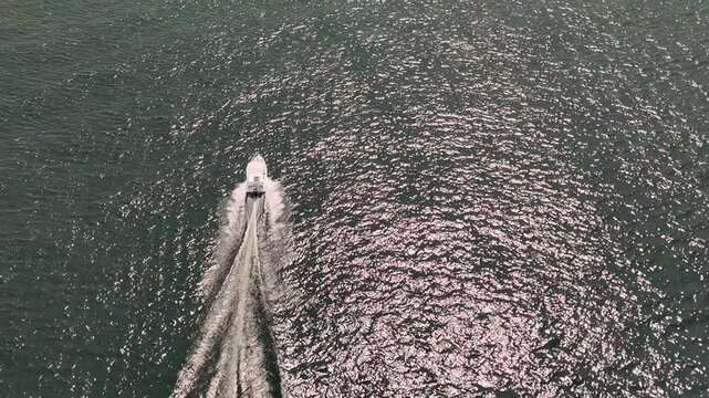 Close drone video of a private luxury yacht cruising across Lake Maggiore, Italy, under bright midday sun, leaving white trails on the deep blue water. Northern Italy