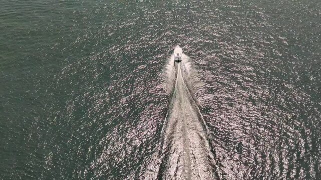 Close drone video of a private luxury yacht cruising across Lake Maggiore, Italy, under bright midday sun, leaving white trails on the deep blue water. Northern Italy