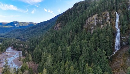 Aerial view of a waterfall cascading down a rocky cliff face surrounded by a dense evergreen forest
