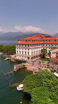 Drone video of Isola Bella&rsquo;s Borromeo Palace seen from the lake. Elegant red-roofed estate rises above the water, surrounded by Alpine peaks, lush gardens, and sparkling Lake Maggiore, Italy