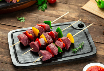 Veal shish tawook skewers with vegetables, ready for grilling, wooden surface.