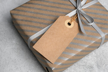 Gift box wrapped in brown paper with silver stripes, tied with gray ribbon and a blank kraft tag,...