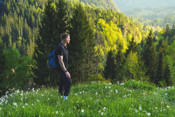 Hiker standing in blooming alpine meadow with forested hills in Triglav National Park, Slovenian Alps