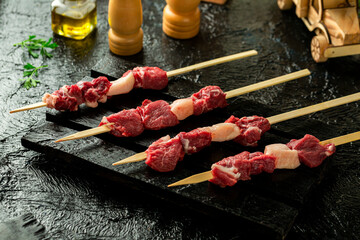 Fresh veal chunks with fat, skewered and ready for grilling, black background.