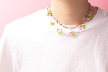 Multicolored handmade chains made from beads and natural stones on a woman in a white t-shirt in front of pink background.