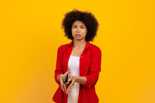 Poverty and absence of money. Upset african american woman demonstrating empty wallet, sad black female searching for cash, standing isolated over yellow studio background, copy space