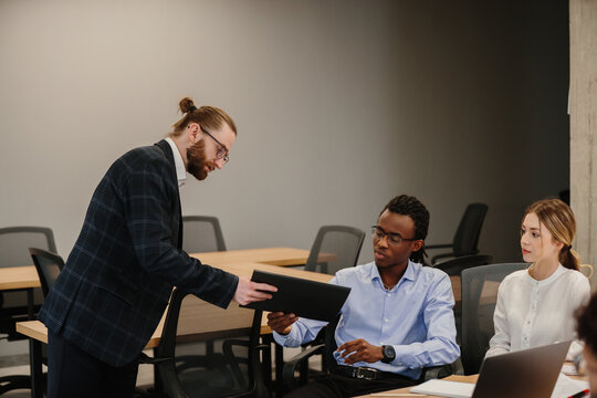Businessman giving digital tablet to young african american colleague in meeting room - Powered by Adobe