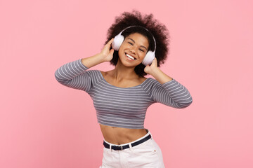Stylish young African American woman dancing with headphones on, positive black female enjoying...