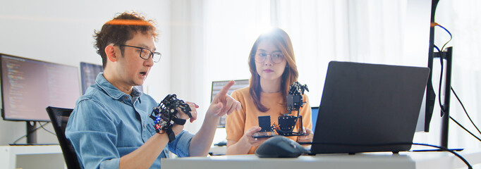 Asian male, female programming developer work together at home office, coding robotic arm machine. Information technology, software engineer programmer job, man woman coworker teamwork. Copy space