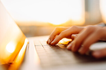 Close-up of young business woman's hands typing on a keyboard in the sunset. Female freelancer...
