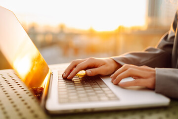 Close-up of young business woman's hands typing on a keyboard in the sunset. Female freelancer...