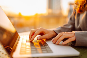 Close-up of young business woman's hands typing on a keyboard in the sunset. Female freelancer...
