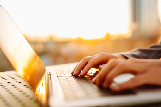 Close-up of young business woman's hands typing on a keyboard in the sunset. Female freelancer working on a laptop and enjoying the sunset. Business concept.