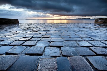 Cobblestone pier vanishing point towards dramatic sunset over the ocean under brooding skies, a captivating tranquil landscape.