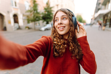 Selfie time! Young woman with headphones taking selfie and blogging while walking through the city...