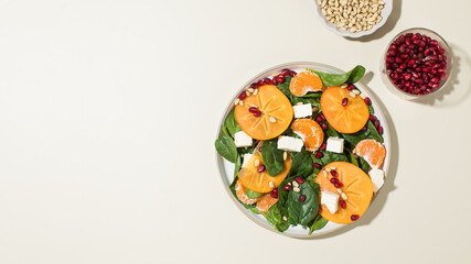 Winter salad. Fresh persimmon and pomegranate spinach salad with feta and pine nuts. Copy space