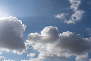 Fluffy white clouds drift across a vibrant blue sky under bright daylight. The sun shines brightly, creating a serene and inviting atmosphere. Perfect for a calm day outdoors.