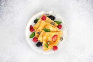 Thin pancakes or crepes with berries on a white plate, on a gray background. Top view. Breakfast food.