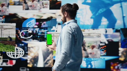 Young adult holds phone with chroma key screen and connecting on socials, using his imagination and modern e commerce skills to connect with people online. Entertainment. Camera B.