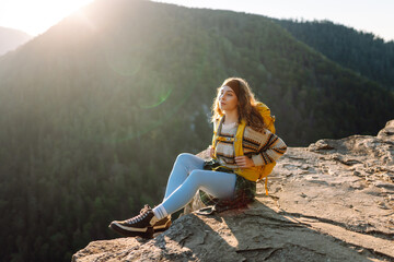 Beautiful woman hiker feels freedom standing on rocky ledge enjoying sunset in mountains. Young...